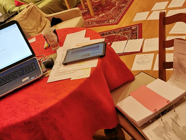 Laptop, Tablett und Papiere am Tisch, bzw. Unterlagen am Boden